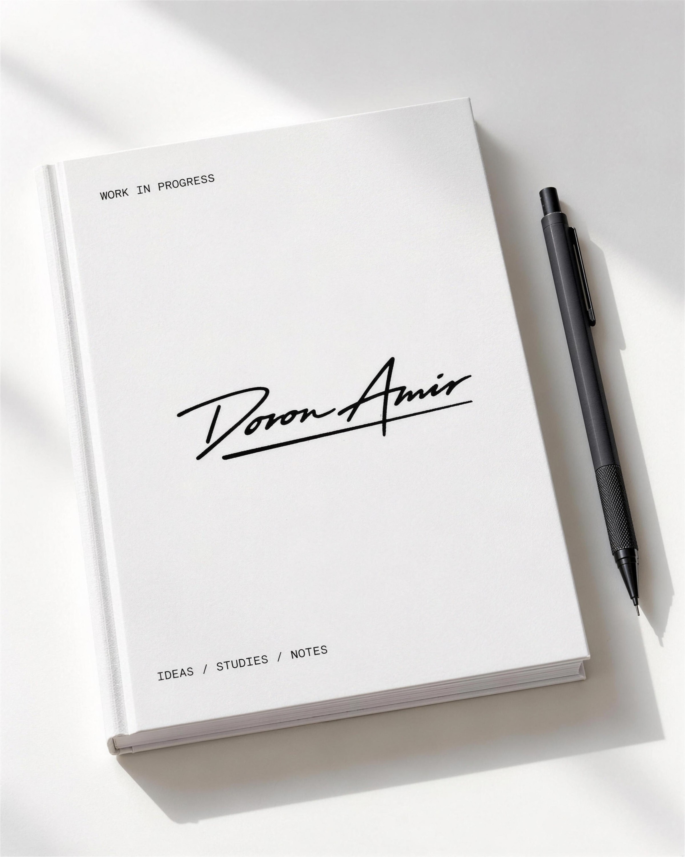 White notebook with the Doron Amir signature on the cover and a black pen